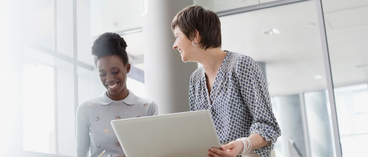 two businesswomen laughing while looking at their laptops